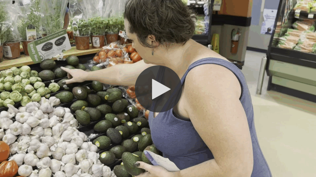 A woman in Maine choosing produce at a grocery store with a video play button over it.